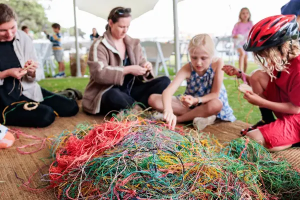 Group of adults and kids weaving an artwork