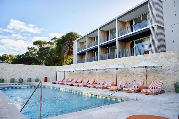 Outdoors pool with orange striped pool lounge chairs and The Lodge Wadjemup hotel behind.