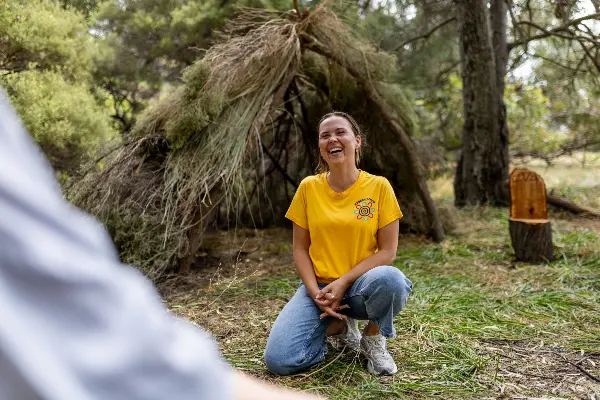 Koorda's Crew presenter sitting on the ground next to a traditional Aboriginal shelter (maya maya).