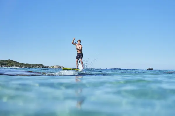 Person on a stand-up paddleboard gliding across turquoise water under a clear blue sky.